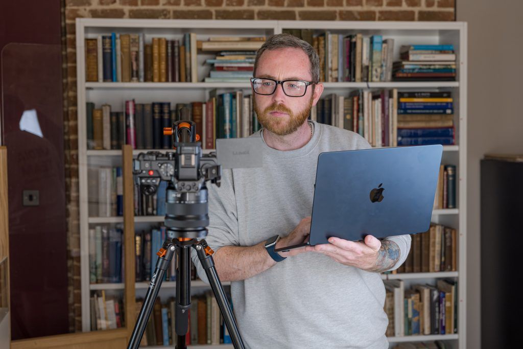 Male holding laptop and looking at photography camera