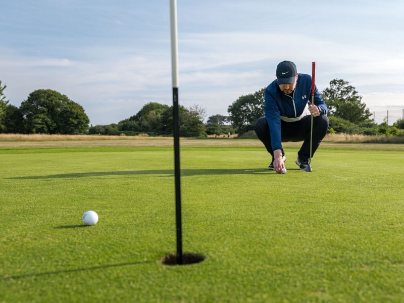 Male lining up putt with another ball next to hole